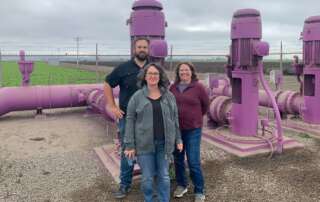 Three people standing in front of purple water pipes